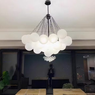 Modern chandelier hanging in a room with a table and plants.