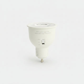 A white GU10 LED projector light bulb lying on a dark, textured gray surface.