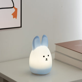 Cute rabbit-shaped night light on a table with books and a framed picture in the background.