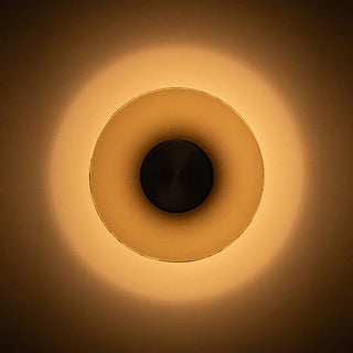 A minimalist circular wall sconce with a warm glowing light, featuring concentric rings in a warm golden-brown gradient against a dark background.
