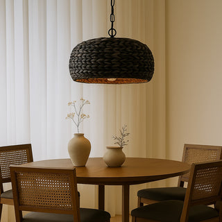 Black woven water hyacinth pendant light hanging above a round wooden dining table with rattan chairs in a warm, neutral-toned room featuring ceramic vases and soft ambient lighting.