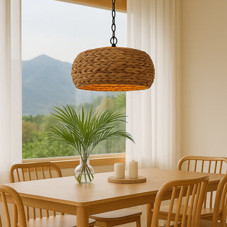 Natural woven water hyacinth pendant light hanging above a timber dining table with rattan chairs in a bright, coastal-style room featuring neutral tones and mountain views through large windows.