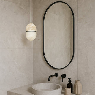 Bathroom with oval mirror, sink, and decorative items on a neutral tiled wall.