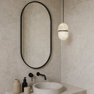 Bathroom with oval mirror, sink, and decorative items on a neutral tiled wall.