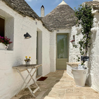 Trulli house exterior with a small table, potted plants, and a white basin.