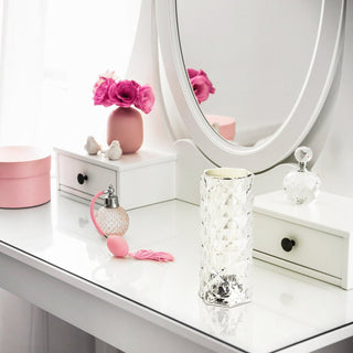 White vanity table with pink decorative items and a gray chair in a bright room.