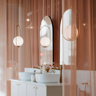 Bathroom vanity with white cabinets, sink, and decorative mirrors with gold frames. Soft pink curtains in the background.