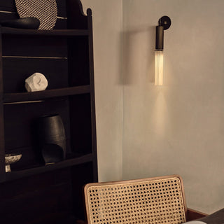 Wall-mounted light fixture casting a warm glow on a wall next to a dark wooden shelf with decorative items.