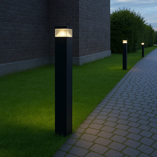 Black outdoor bollard lights on grass next to a brick wall and pathway.