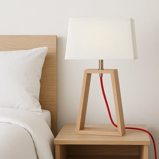 Wooden table lamp with a white shade on a nightstand next to a bed.
