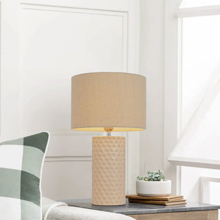 Beige table lamp on a desk with a plant and books in a room setting