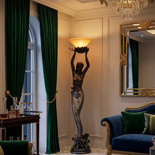 Decorative mermaid floor lamp with both arms raised supporting an upward-facing bowl shade. Features a detailed scaled tail and wave-inspired base. Total height 186cm with a 41cm shade diameter. Accommodates one E27 globe, maximum 60W. A statement piece for living rooms and entrance halls.