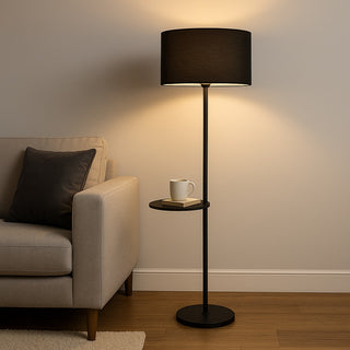Mila Black floor lamp with a cup on a small round table next to a beige sofa in a living room.