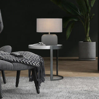 Modern living room with gray armchair, ottoman, and side table against a dark wall.