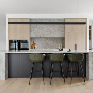 Modern kitchen with light wood cabinets, marble countertops, and gray stools.