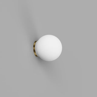 Wall-mounted light fixture with a white globe and brass base on a gray background