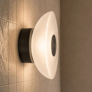 Modern wall-mounted light fixture with a frosted white dome-shaped shade and a matte black cylindrical base, shown lit against a beige tiled wall.
