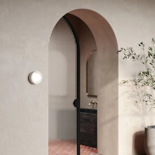 Archway leading to a bathroom with a black door and light fixture on the wall.